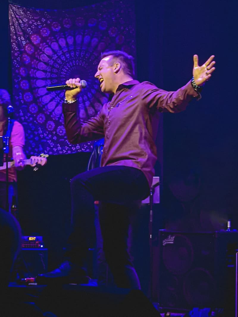 Garry Hall singing on stage with one arm outstretched